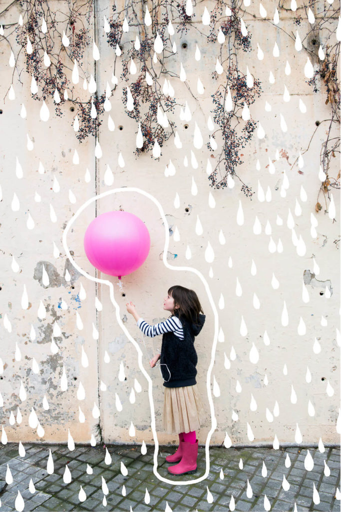child holding a large pink balloon with creative artwork of raindrop doodles on the wall behind
