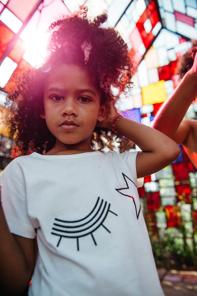 Young girl with curly hair posing in front of a colorful stained-glass backdrop