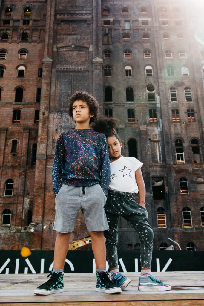 Young boy dressed as a superhero with a blue cape, holding a large blue number three balloon at a birthday party.