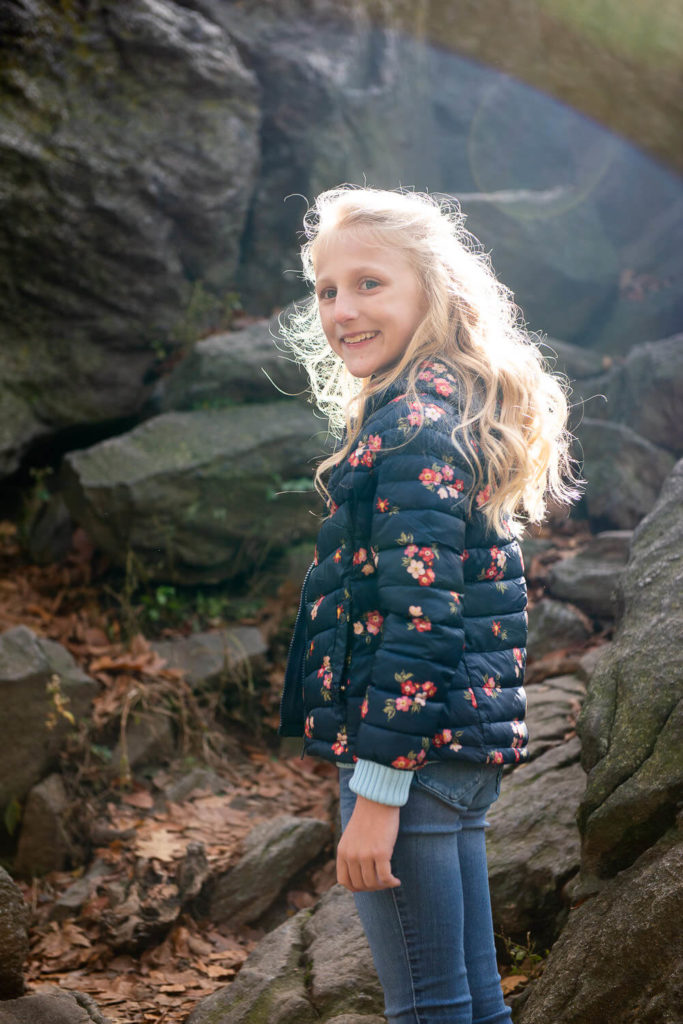 Girl holding a bouquet of wildflowers, standing in a field with tall grasses under a sunny sky.