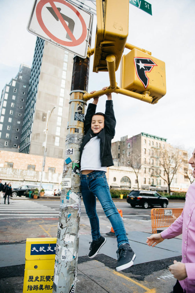 Boy hanging playfully from a city street sign with a smile.