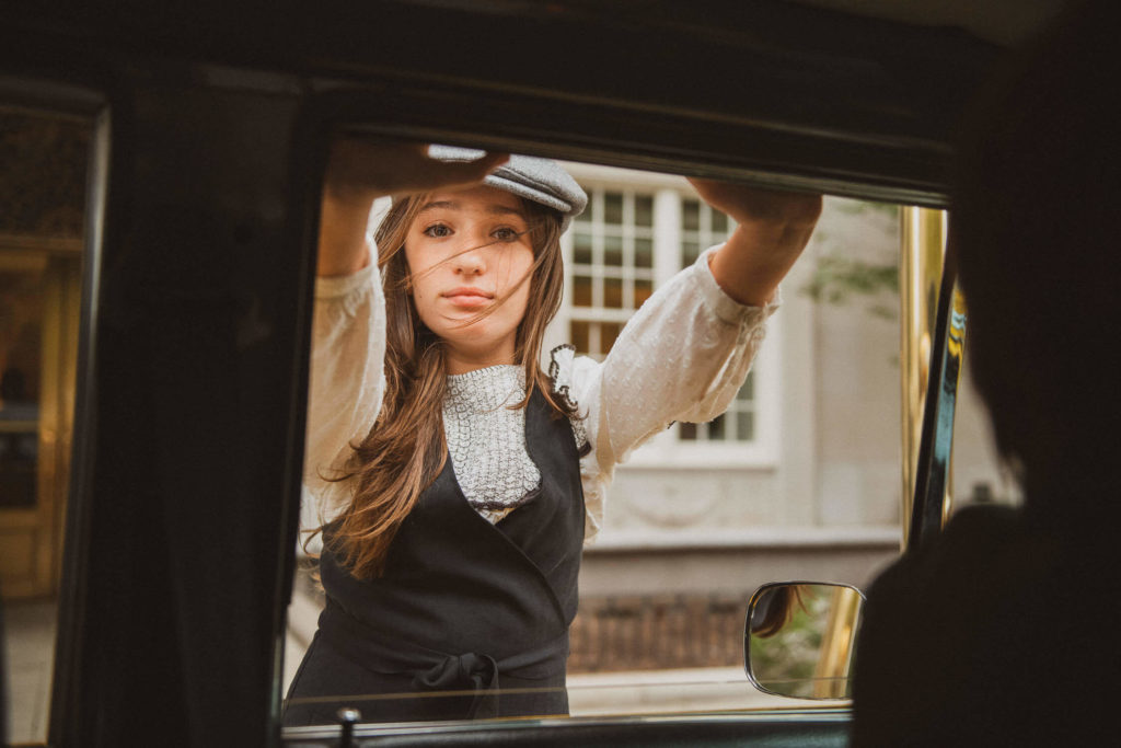 girl looking through a car window with a curious expression, wearing a newsboy cap