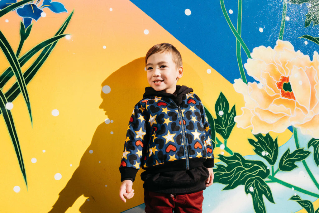 Boy in a colorful jacket with a bold yellow and blue mural background.