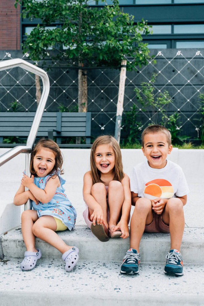 Three kids smiling and sitting by the poolside, capturing a joyful summer moment.