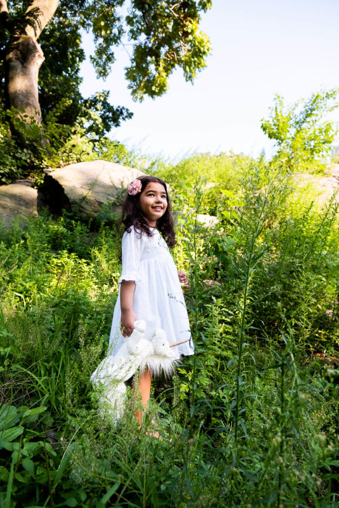 Toddler in a white outfit and birthday hat, playing near a set of colorful toys in a minimalistic room.