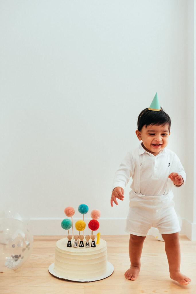 toddler in a party hat walking around a minimalist room with colorful toys on the floor