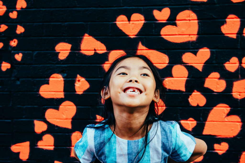 Girl smiling in front of a mural of red and black heart shapes.