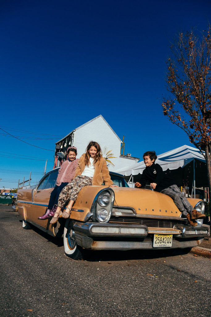 three children sitting on an old vintage car under a clear blue sky, playful and retro family moment