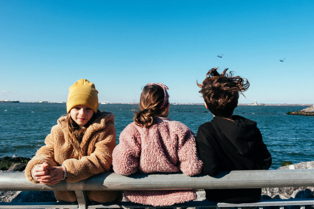 three kids sitting on a pier bench, looking out over the water with windy hair