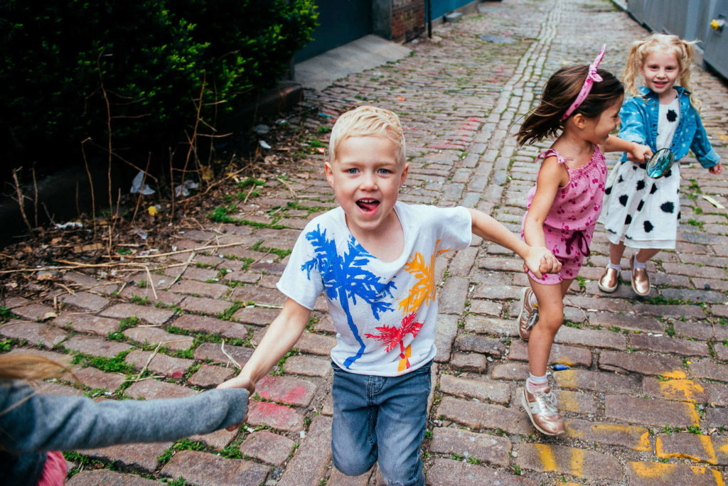 kids holding hands and running down a cobblestone path, joyful expressions during a lively outdoor moment