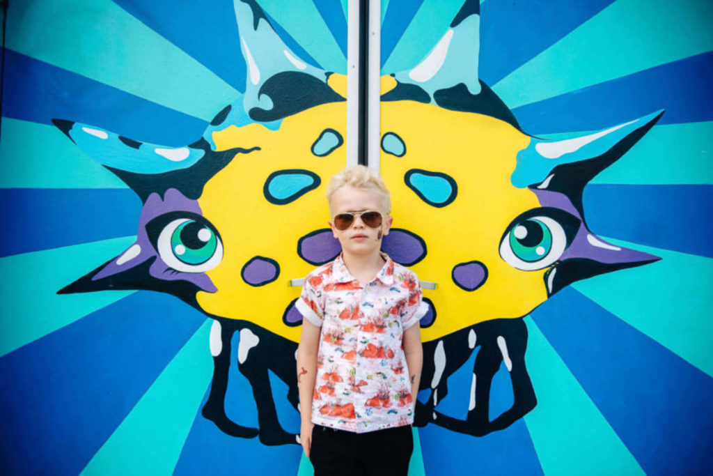 boy posing confidently with sunglasses in front of a vibrant street mural