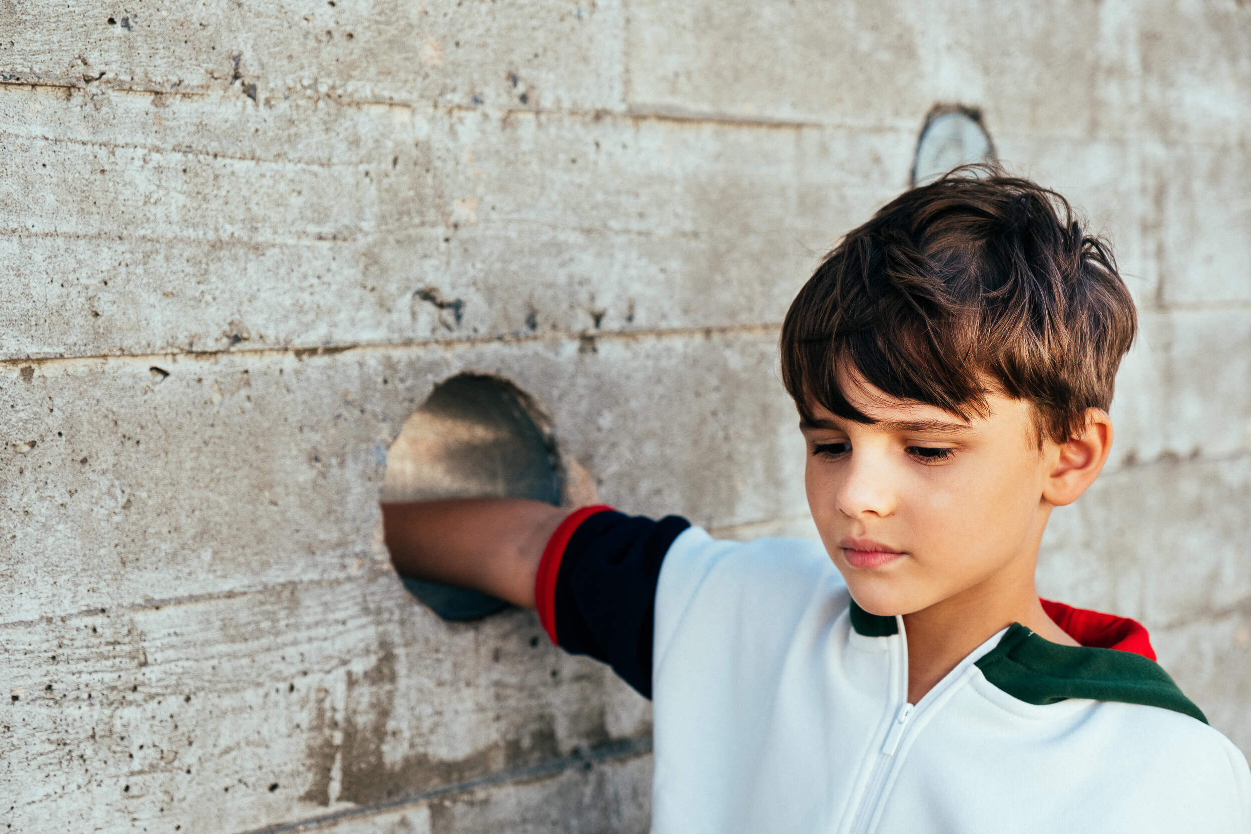 boy with thoughtful expression placing his hand in a circular hole on a concrete wall