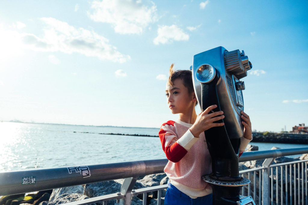 girl holding a binocular viewer by the water, gazing out over the horizon on a sunny day