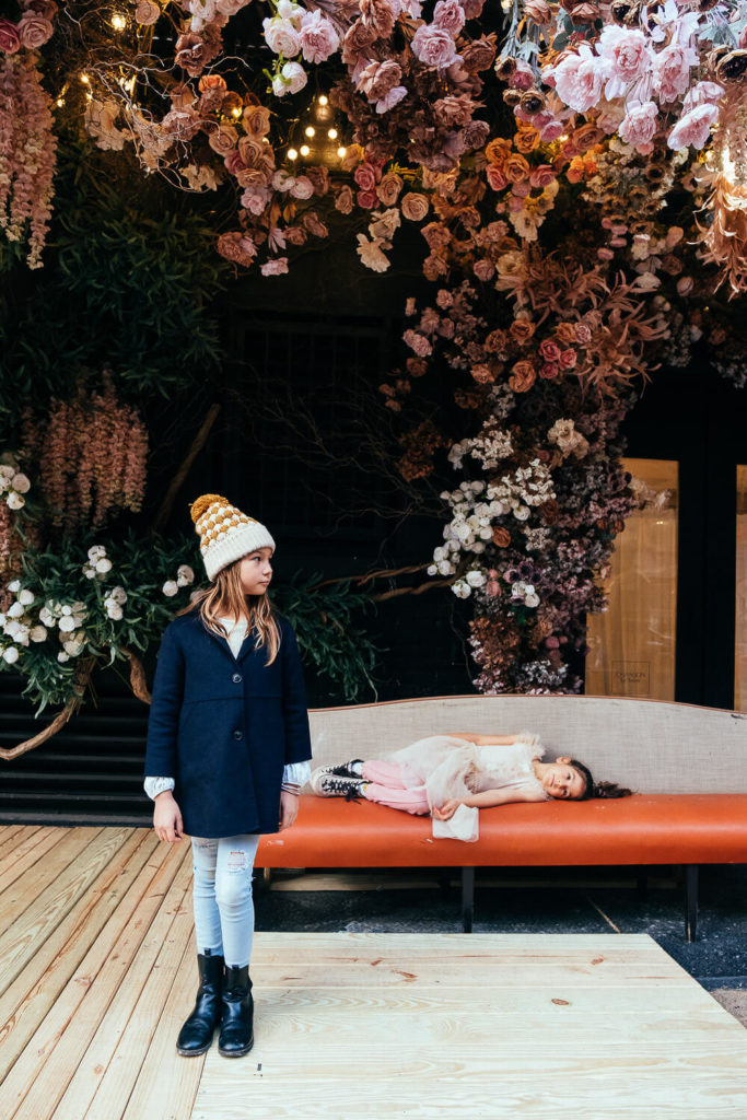 Two kids, one standing and one lying on a couch, in a floral-decorated room