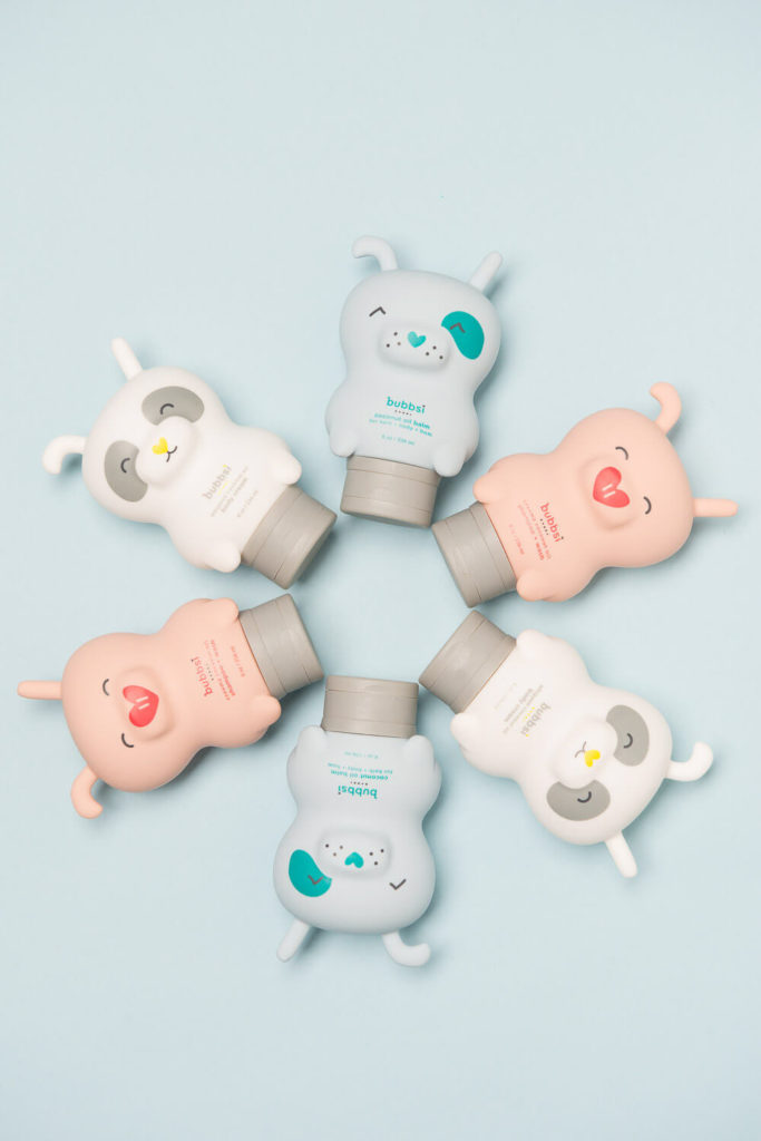 Six pastel-colored, bear-shaped bottles of body lotion are arranged in a circle on a light blue background. With cute facial expressions in gray, blue, and pink shades, this delightful composition exemplifies brand photography at its finest.