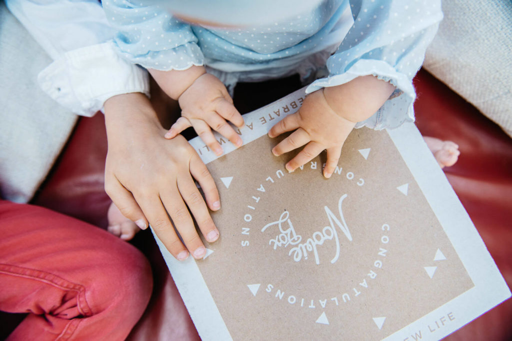 A baby gently touches a brown cardboard box with white text that reads 