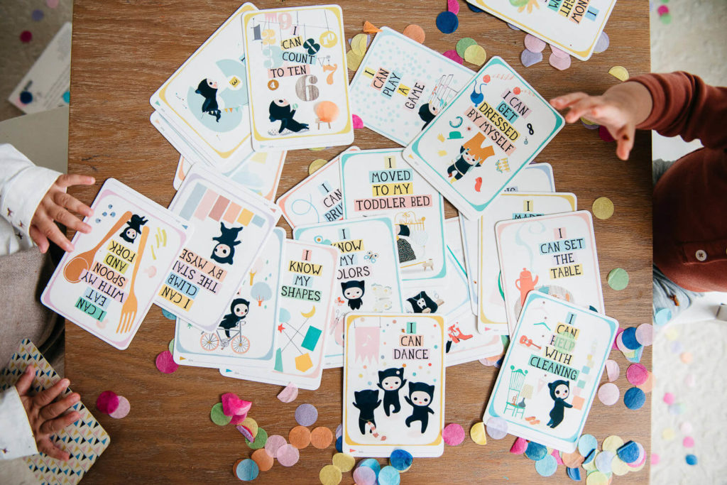 A collection of colorful milestone cards, captured through vibrant commercial photography, features playful illustrations and captions like 