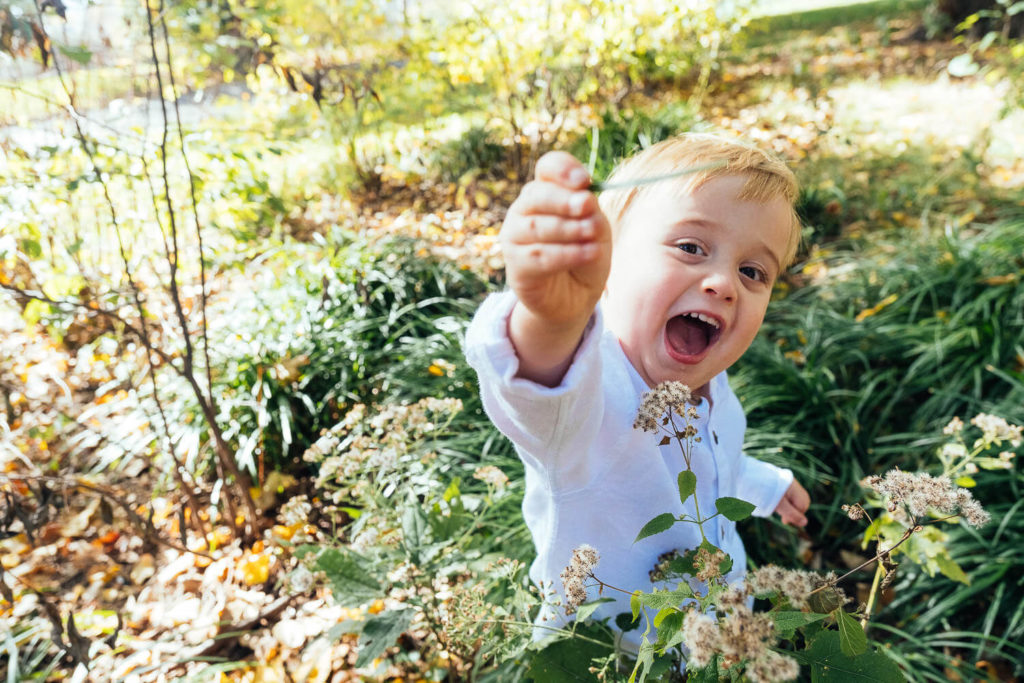 Smiling child holding a flower and reaching towards the camera in a garden setting
