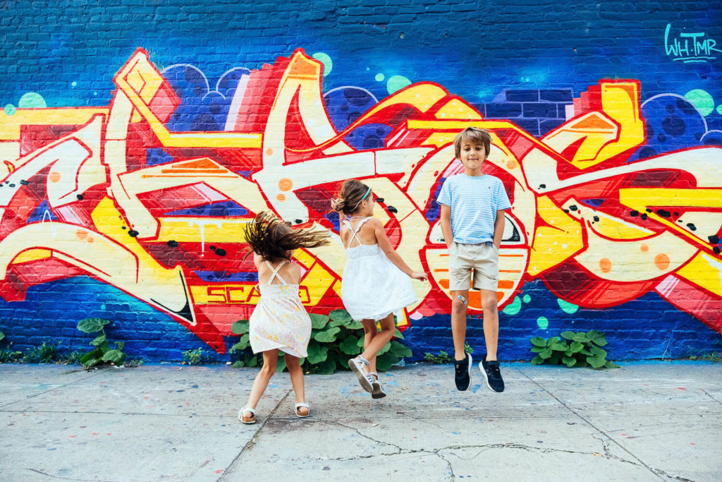 three kids jumping in front of a colorful graffiti wall, expressing joy and energy