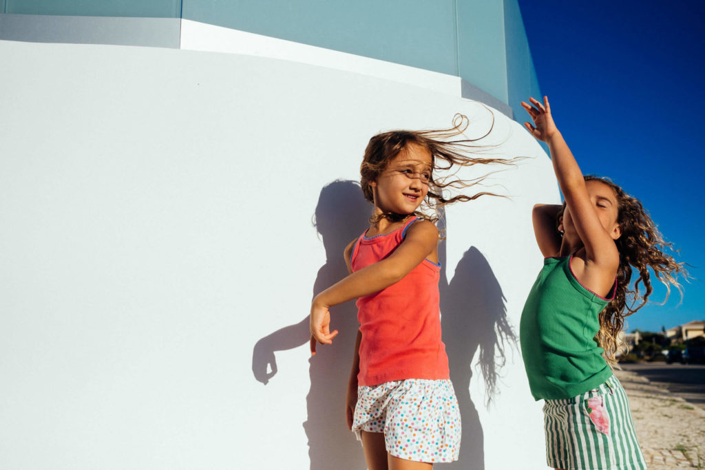 Two girls playing with shadows on a white and blue architectural backdrop