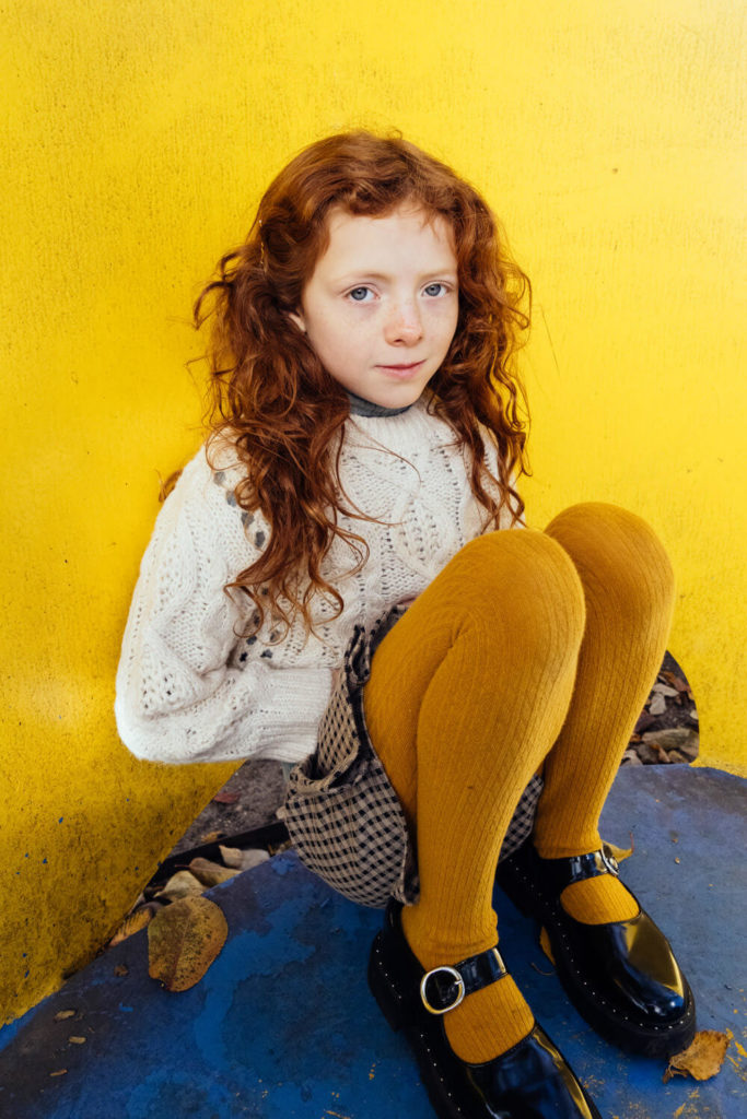 Red-haired girl in yellow tights sitting against a vibrant yellow background
