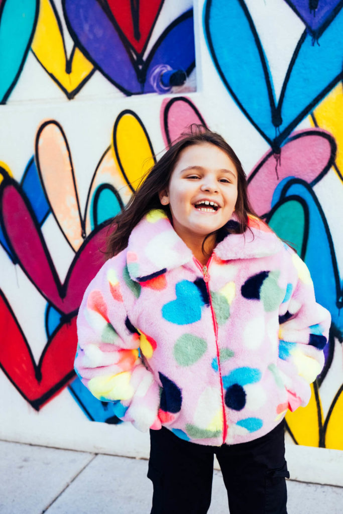 girl posing with yellow bike and graffiti heart backdrop, playful kids photography