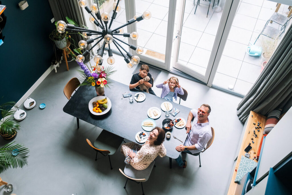 Overhead view of four people sitting around a dining table, smiling and eating together in a modern, brightly lit room—perfect inspiration for family photography NYC.
